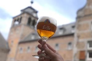 a person holding a glass of beer in front of a building at All you need is Dinant, Leffe, Maredsous and Anhée-sur-Meuse in Anhée