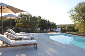 a swimming pool with lounge chairs and an umbrella at Las Huertas del Abrilongo in La Codosera