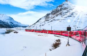 a red train in front of a snow covered mountain at Dimora Perla di Villa - Historical Wine Retreat near Bernina Express in Villa di Tirano
