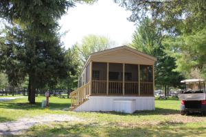 a small building in a park with a car parked next to it at Plymouth Rock Camping Resort Park Model 21 in Elkhart Lake