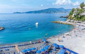 a beach with blue umbrellas and people in the water at Nice Apartment In Zoagli With Wifi in SantʼAmbrogio +15 photos