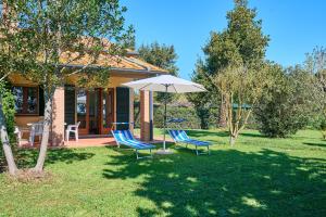 une maison avec deux chaises et un parasol dans la cour dans l'établissement Mare Etrusco Villetta D2, à Populonia