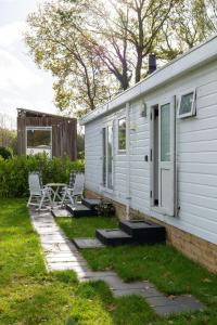 Una casa blanca con dos sillas y un patio. en Chalet Bosgeluk - close to the woods, en Anloo