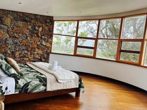 Wandin Farm Views في Gruyere: غرفة نوم بحائط حجري مع سرير ونوافذ