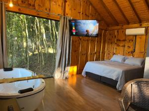 a bedroom with a bed and a tub and a tv at Chalé Refúgio Panorâmico in Canela