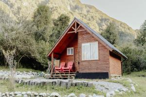 a small cabin with two red chairs on the porch at Cabañas Refugio Río Roberto in Villa Santa Lucía