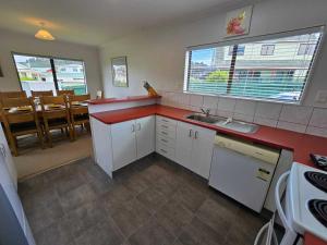 a kitchen with white cabinets and a red counter top at Hosts on the Coast Dinah & Una's Place in Whangamata +13 photos