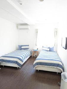two beds in a room with white walls and wood floors at Shima Stay holoholo in Zamami