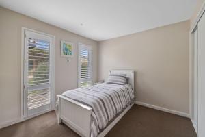ein weißes Schlafzimmer mit einem Bett und zwei Fenstern in der Unterkunft Casa del Mar Phillip Island Ocean Views in Surf Beach