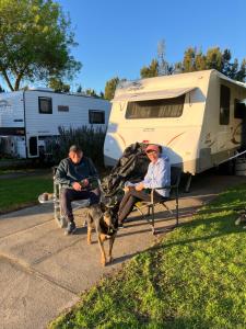 two men and a dog sitting in chairs in front of an rv at Lake Colac Holiday Park in Colac