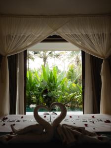 two swans sitting on a bed in front of a window at Alankara Villa & Spa Ubud by Mahaprana in Tegalalang +34 photos