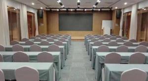 une salle de conférence avec des tables, des chaises et un écran dans l'établissement James Joyce Coffetel Shijiazhuang Wanda Plaza Tangu Metro Station, à Shijiazhuang