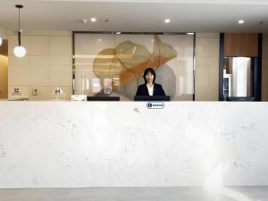une femme assise derrière un comptoir dans un bureau dans l'établissement GreenTree Inn Express Beijing Fangshan District Doudian Road Jin Yuan, à Nanfang