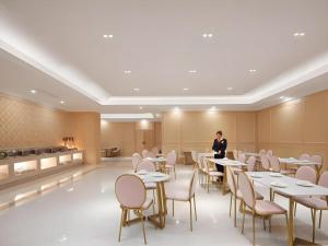 a woman standing in a restaurant with tables and chairs at Vienna Hotel Shanghai Hongqiao Hub National Exhibition Center Huqingping Road in Shanghai