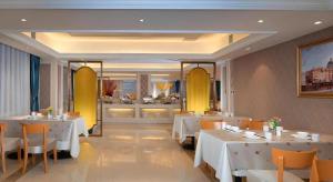 un restaurant avec des tables et des chaises blanches et une cuisine dans l'établissement Vienna Hotel Jilin Dunhua High-Speed Railway Station, à Dunhua