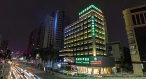 a tall building with green lights on it at night at GreenTree Inn Zhongshan West District Fuhua Road Branch in Zhongshan