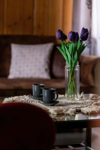 eine Vase mit lila Blumen auf einem Tisch mit zwei Tassen in der Unterkunft Spacious House For Families Szczyrk in the Mountains by Noclegi Renters in Szczyrk