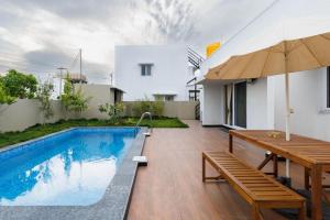 a swimming pool with a wooden table and a bench and an umbrella at The Garden Retreat by StayJadePool2BHKLawn in Berikai