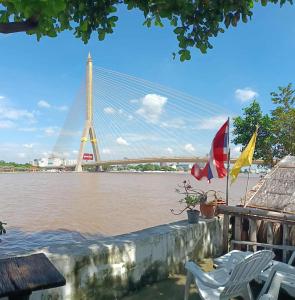 a bridge over a river with two flags and chairs at New Phiman Riverview Guesthouse in Bangkok
