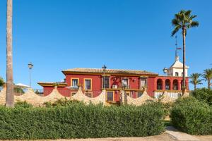ein rotes Haus mit einer Palme und einem Zaun in der Unterkunft Holiday House Dehesa del Colmenar in Cabra