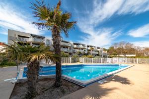 a pool with palm trees in front of a building at Le Rêve les Pieds dans l'eau in La Tranche-sur-Mer