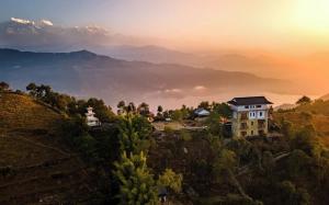 a house on a hill with mountains in the background at Pumdikot Mountain Lodge in Pokhara