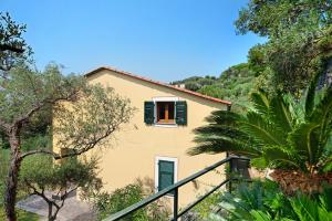a yellow house with green shutters and trees at Villa Ciò in Bonassola