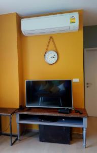 a tv with a clock on a yellow wall at The Valley Escape สองห้องนอน สวย สงบ สบาย in Phayayen