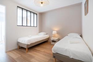 two beds in a white bedroom with a window at L’Escale – Tout à pied à Ste-Marine in Combrit
