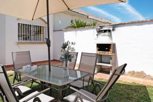 a patio with a glass table and chairs with an umbrella at Chalet Fuente2 piscina común famila in Conil de la Frontera