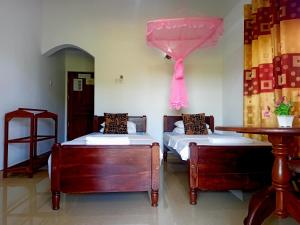 タンガラにあるSunny Side Villaのベッドが2つとピンクのカーテンがかかったテーブルがある寝室