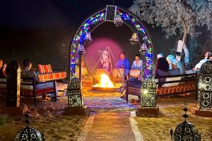 a group of people sitting around a fire at night at Merzouga Best Luxury Camp in Merzouga