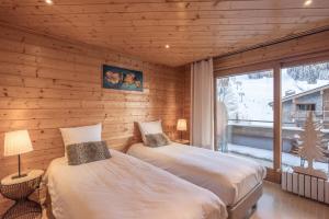 two beds in a room with wooden walls and a window at L'origan in Le Grand-Bornand