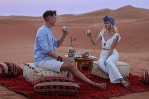 a man and woman sitting in the desert holding wine glasses at Merzouga Best Luxury Camp in Merzouga