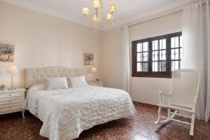 a white bedroom with a bed and a chair at Casa La Perla - Solo Familias in Conil de la Frontera