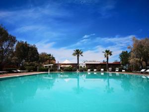une grande piscine bleue avec des palmiers en arrière-plan dans l'établissement Feriendorf Le Tamerici Mobilehome Pirri für 5 Personen, à Marina di Cecina 21 autres photos