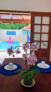 Pousada com café da manhã, piscina, natureza, sossego no Norte da Ilha, Ingleses في فلوريانوبوليس: طاولة مع طبقين و مزهرية مع الزهور الأرجوانية