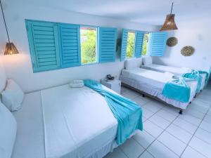 two beds in a room with blue shuttered windows at Amaly Pousada in Japaratinga