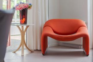 Ein orangefarbener Stuhl steht neben einem Tisch mit einer Vase voller Blumen. in der Unterkunft Duinvilla Deluxe met Sauna en Whirpool - 6 personen in Holle Poarte