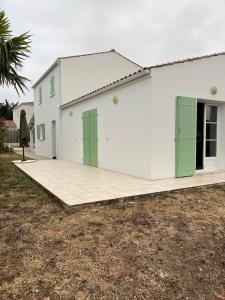 een wit gebouw met groene deuren en een tuin bij Villa les Mésanges 5 min from the beaches in Vaux-sur-Mer