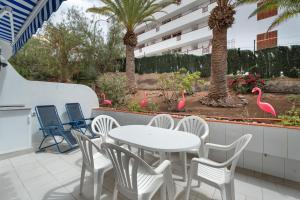 Un patio con una mesa y sillas blancas y palmeras. en Apto Jardin del Sol Beach, en Puerto de Santiago