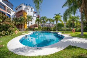 a swimming pool with palm trees and a building at Apartamento Coral in Almuñécar