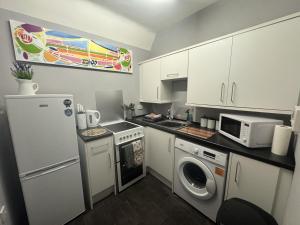 una pequeña cocina con armarios blancos, lavadora y secadora. en The Cosy Neuk, Hawick, en Hawick