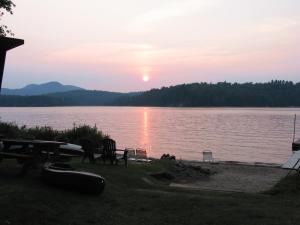 Journeys End Lodging Cabins في Long Lake: غروب الشمس فوق بحيرة مع طاولة نزهة وكراسي +29 صورة