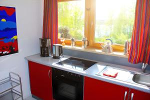 eine Küche mit roten Schränken, einem Waschbecken und einem Fenster in der Unterkunft Haus am See in Illmensee