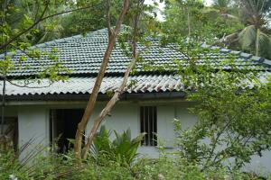 a white house with a gray roof and trees at Sri Vishwa Buddha MUni in Kalagedihena