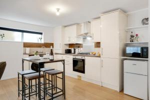 een keuken met witte kasten en een tafel met krukken bij Bright 1-Bed Flat, Near Station, Fast Wi-Fi in Wellingborough
