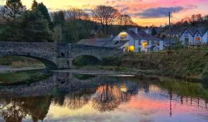 a bridge over a river with houses and a sunset at The Black Lion in Llanfair Talhaiarn