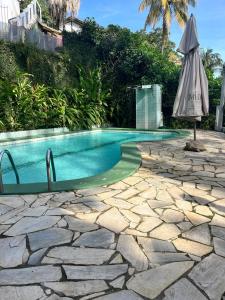 a swimming pool with an umbrella next to a stone patio at Ótima casa próxima a praia e o centro in Ilhabela +15 photos