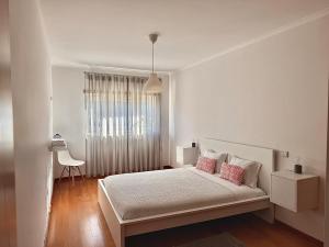 ein weißes Schlafzimmer mit einem Bett mit rosa Kissen in der Unterkunft Nazaré Beach Apartments in Nazaré